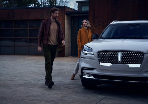 A man and a woman approaching a 2024 Lincoln Aviator® SUV, which illuminates certain lights when they are close | Lincoln of Coconut Creek in Coconut Creek FL