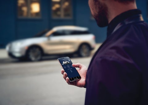 A person is shown interacting with a smartphone to connect to a Lincoln vehicle across the street. | Lincoln of Coconut Creek in Coconut Creek FL