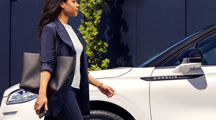 A woman approaches a 2024 Lincoln Corsair® SUV while holding a smartphone. | Lincoln of Coconut Creek in Coconut Creek FL